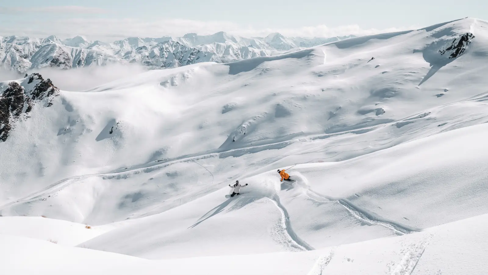 Two skiers carving fresh tracks through deep powder on a wide alpine slope.