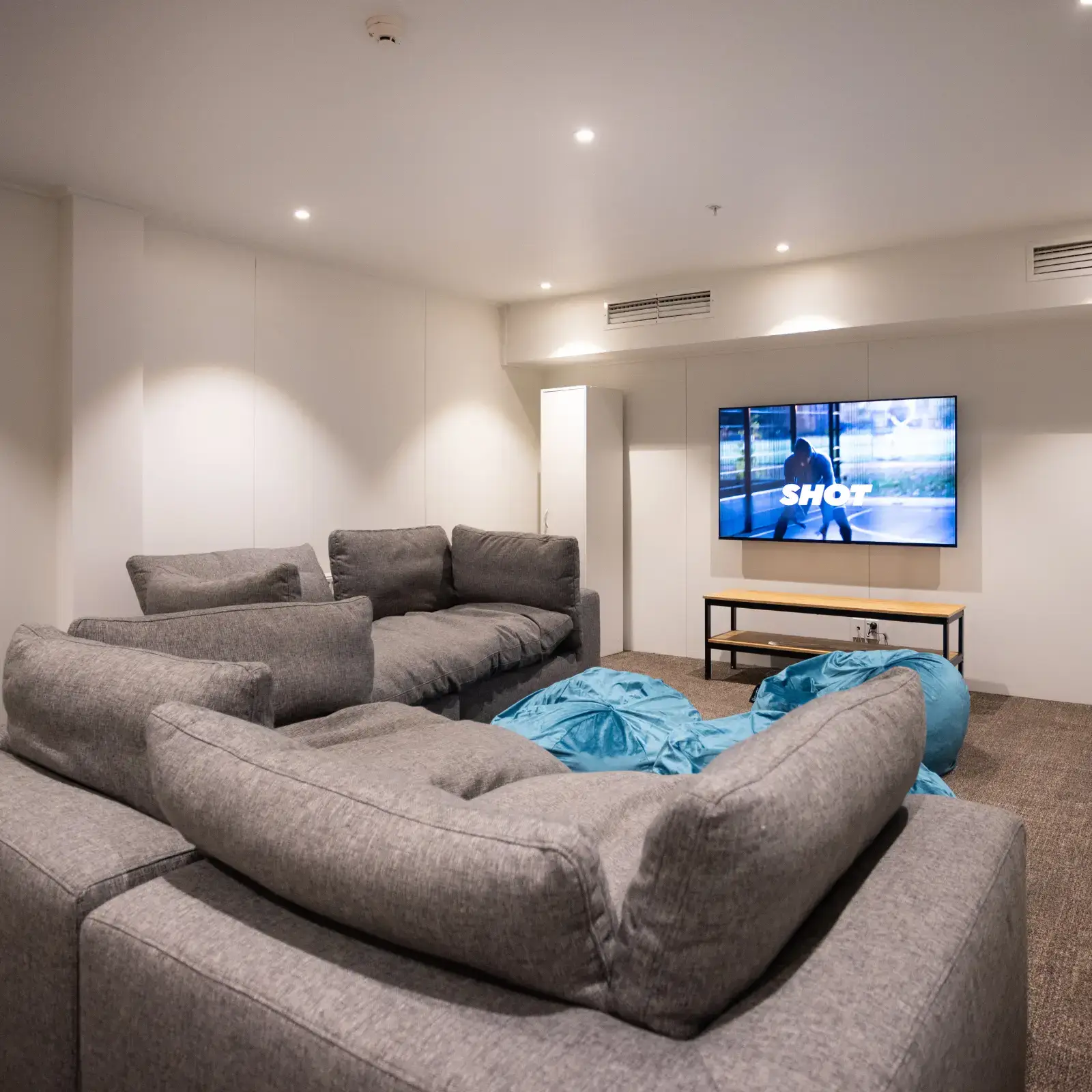 A cosy lounge room in a hostel with large grey coaches and a TV.