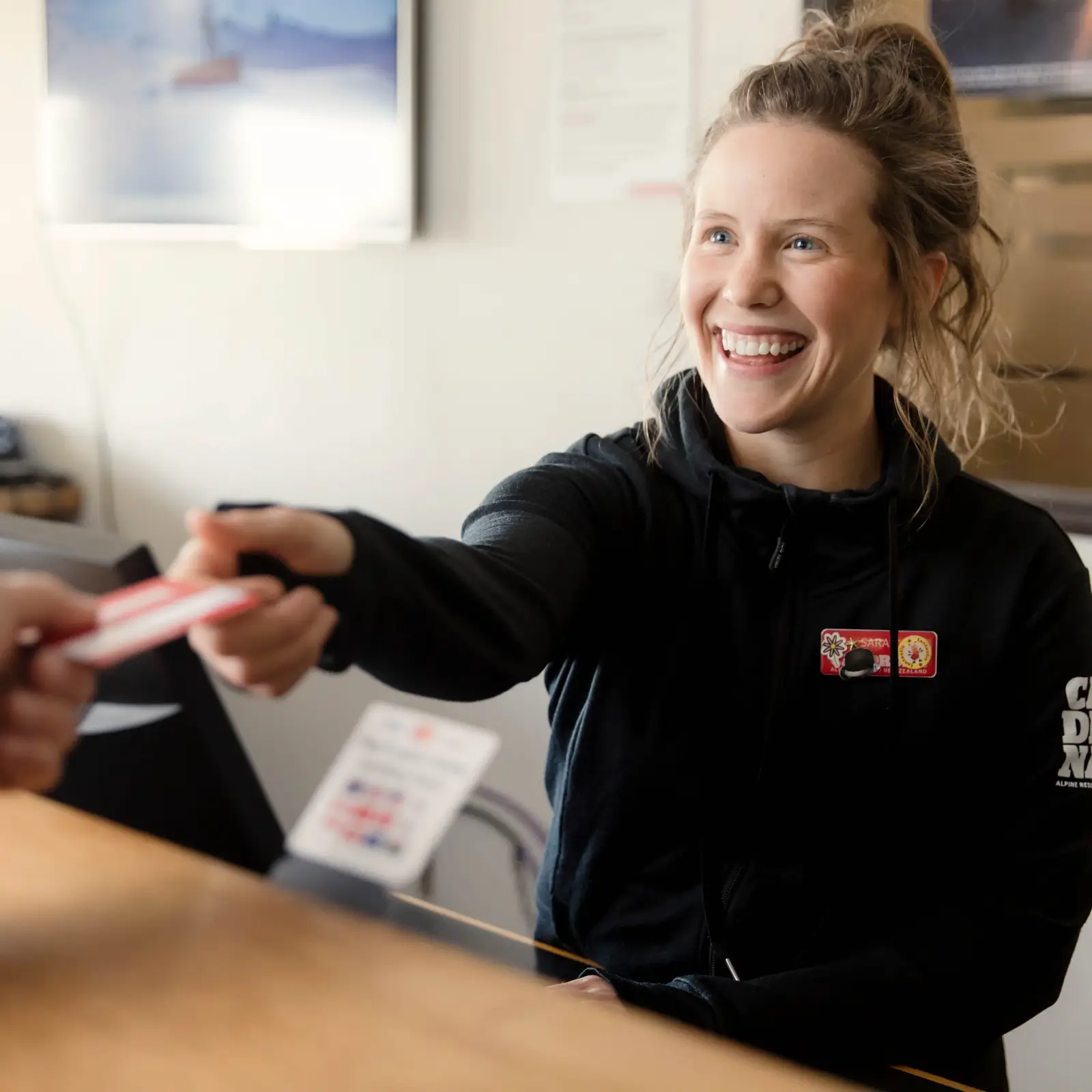 A smiling staff member at Cardrona Alpine Resort hands a lift pass to a guest at the ticket counter, ensuring a smooth start to the ski day.